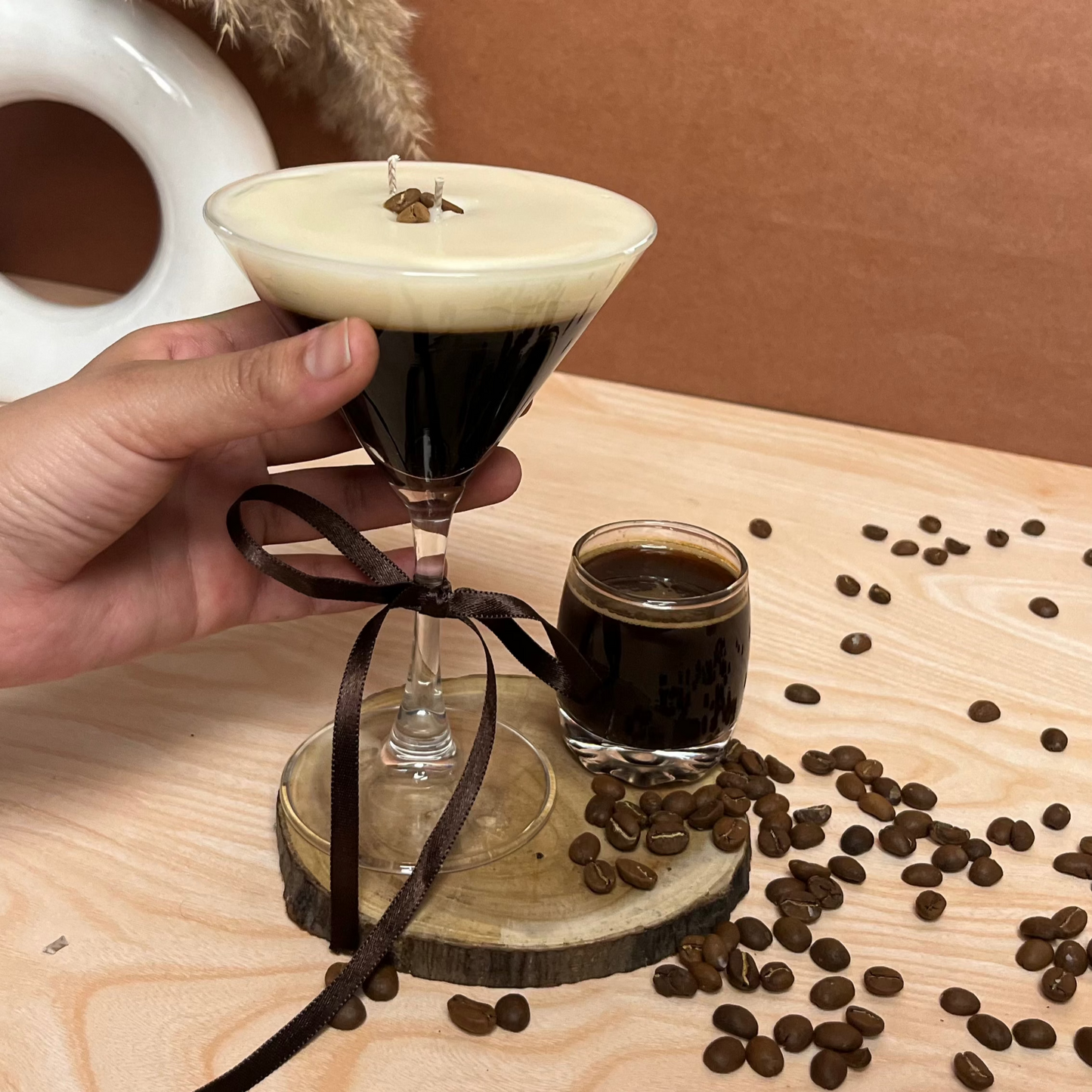 A glass candle designed to look like an Espresso Martini, with a coffee cocktail theme, held in a hand.