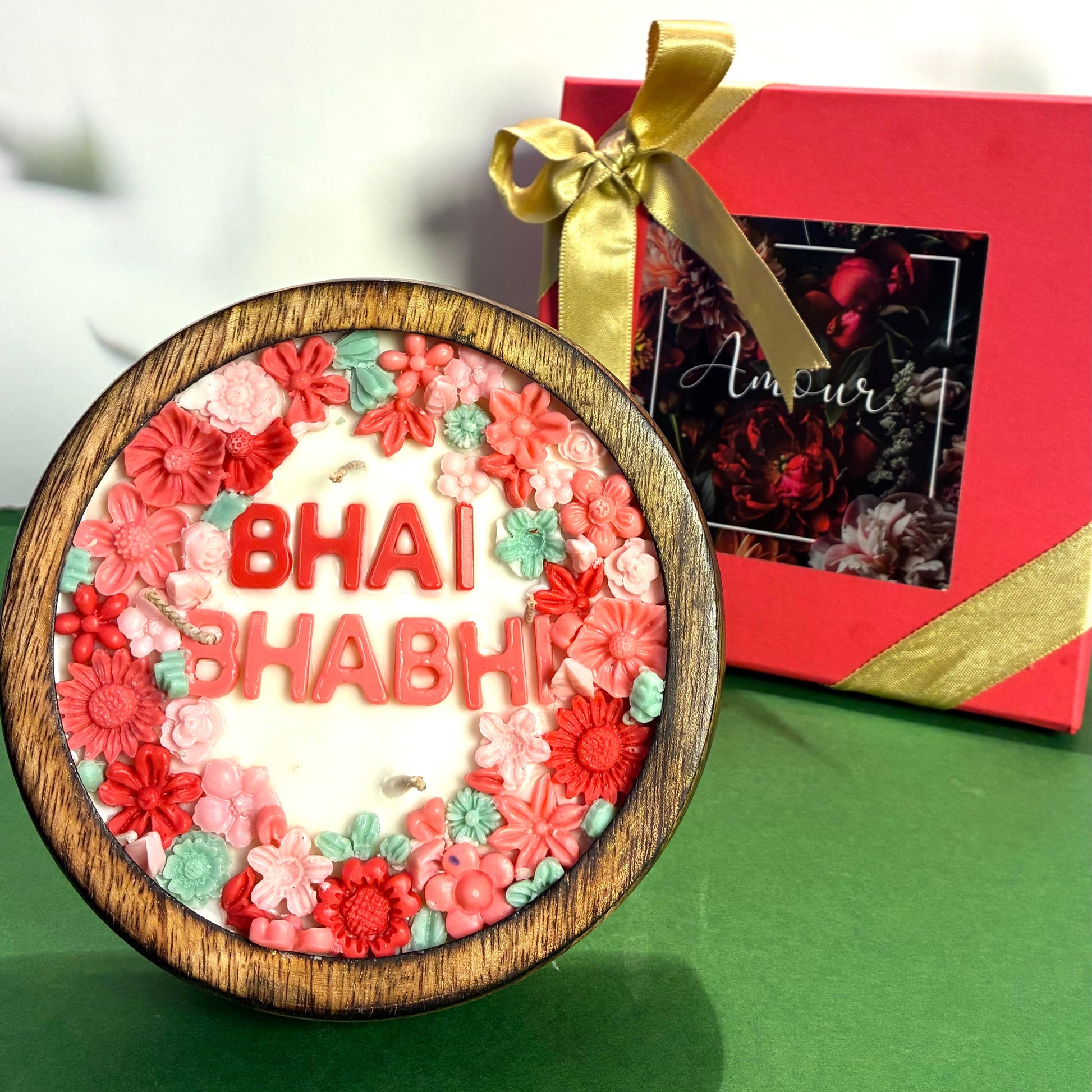 Decorative item with 'Bhai Bhabhi' text and floral design, tied with a gold ribbon, on a green background.