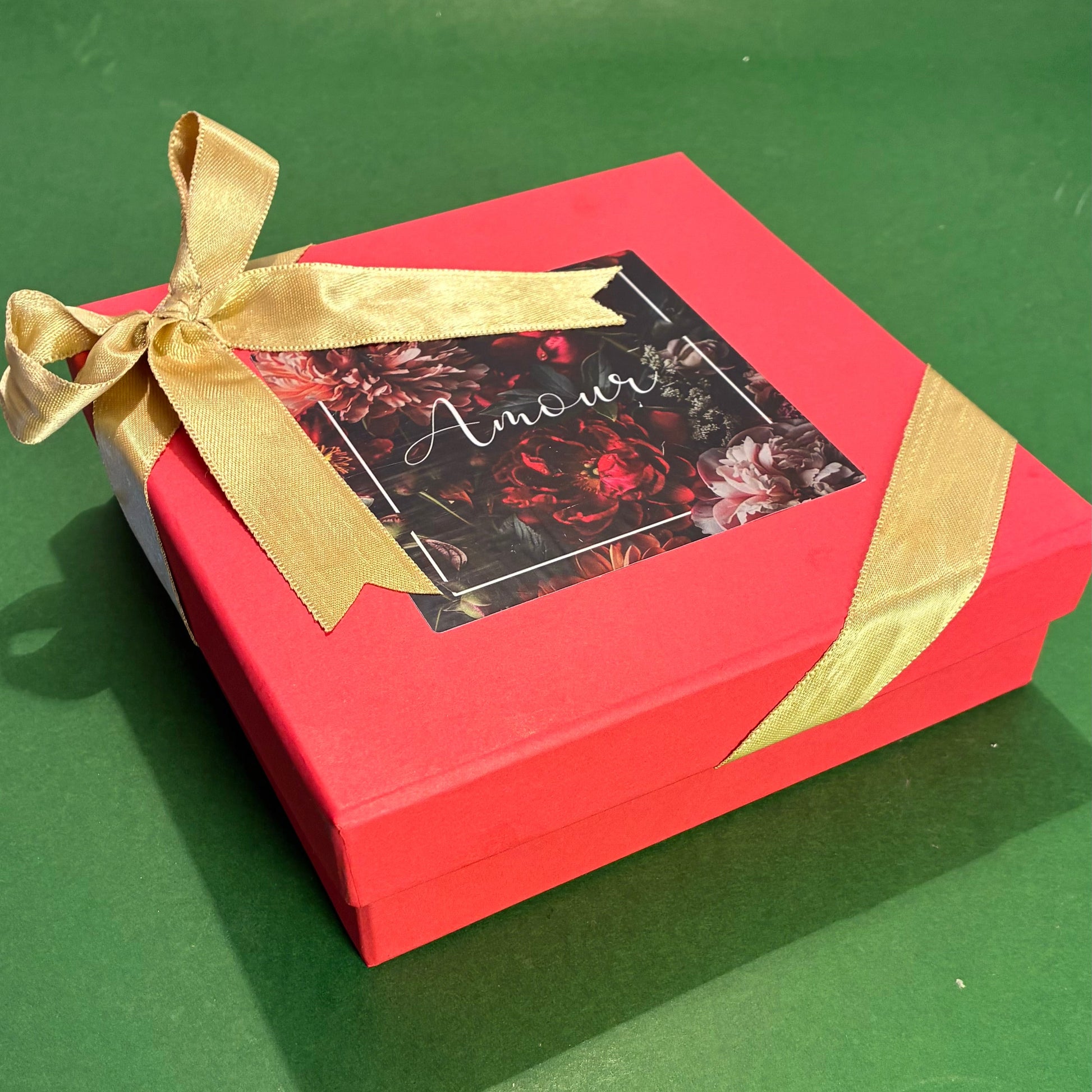 Red gift box with a gold ribbon on a green surface