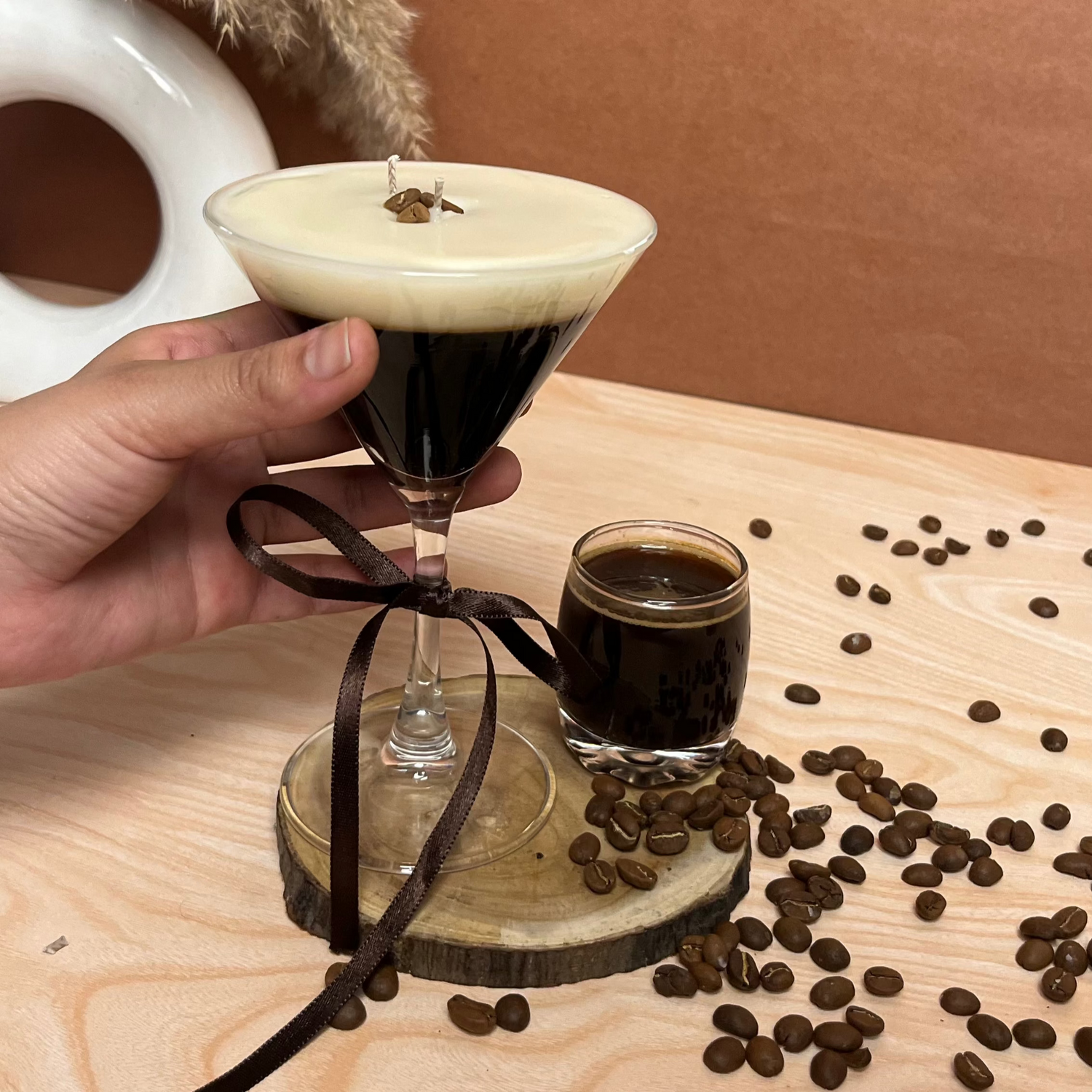 A glass candle designed to look like an Espresso Martini, with a coffee cocktail theme, held in a hand.